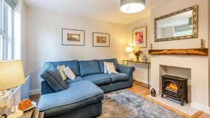 A living room with a blue sofa, fireplace, framed pictures, and a lamp. - 2 Bed in Holt (oc-2377) (Holt)