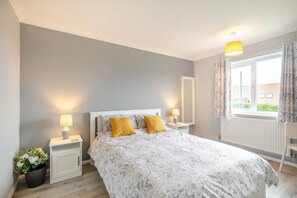 A bedroom with a bed, two bedside tables, a nightstand, a window with curtains, and a potted plant.