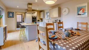 A modern kitchen with a central island, wooden chairs, and a dining table set for breakfast. - 4 Bed in Holt (oc-y27156) (Weybourne)