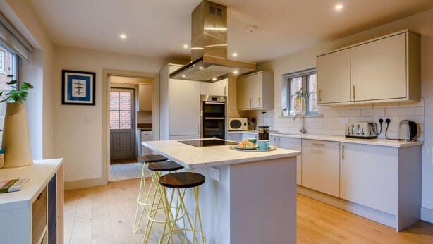 A modern kitchen with a central island, bar stools, and a built-in oven. - 4 Bed in Holt (oc-y27156) (Weybourne)