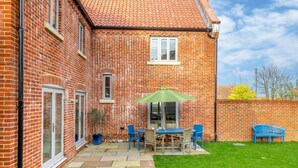 A brick house with a patio, a table with chairs, and a green umbrella. - 4 Bed in Holt (oc-y27156) (Weybourne)