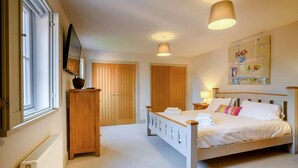 A bedroom with a bed, a wooden wardrobe, a radiator, and a painting on the wall. - 4 Bed in Holt (oc-y27156) (Weybourne)