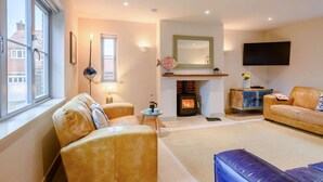 A living room with a fireplace, sofas, a TV, and a window. - 4 Bed in Holt (oc-y27156) (Weybourne)