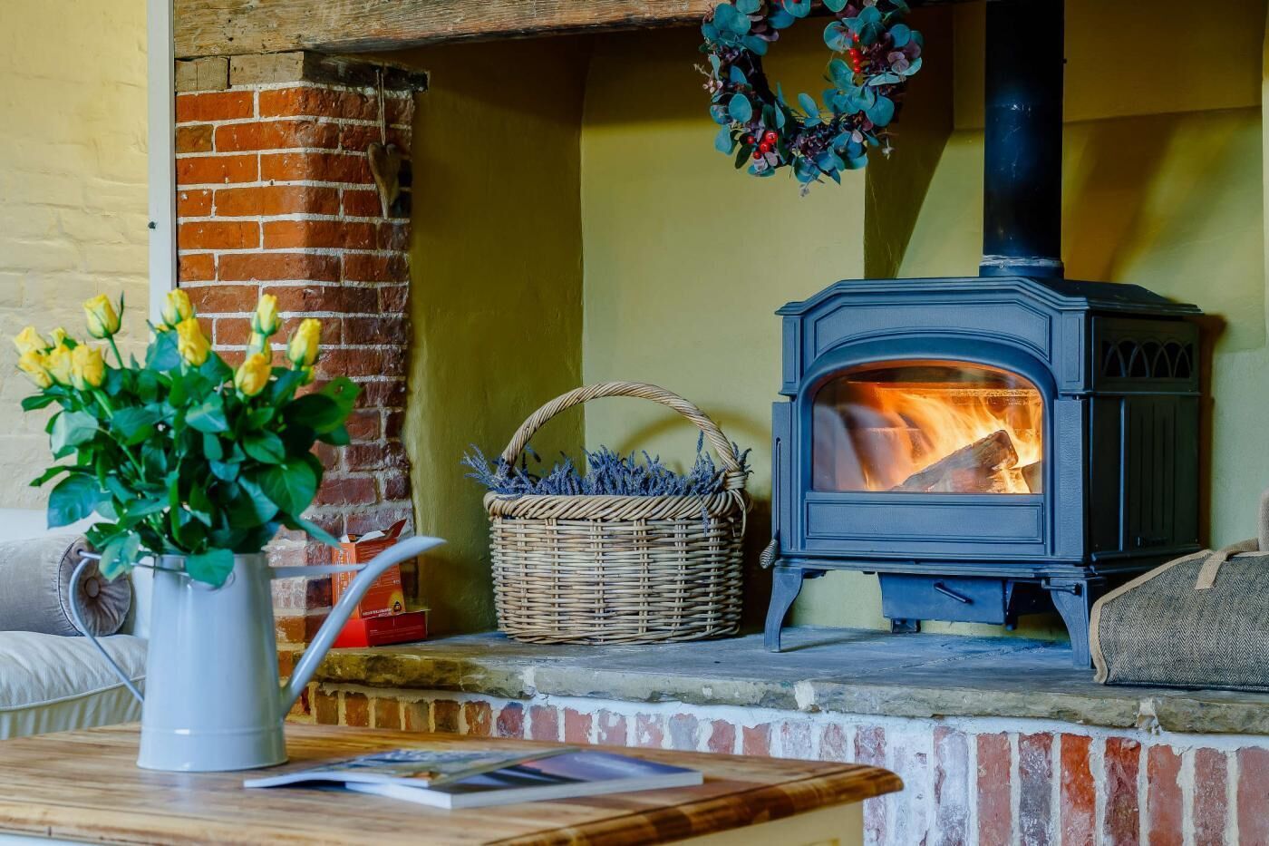 A cozy room with a brick fireplace, a wicker basket, and a vase of yellow flowers on a wooden table.