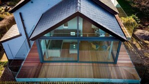 A modern house with a sloped roof, large glass windows, and a wooden deck. - 2 Bed in Morston (oc-2382) (Morston)
