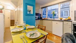 Ein Essbereich mit Tisch für vier Personen, eine Küche mit weißen Schränken, ein Fenster mit Aussicht und eine blaue Akzentwand.