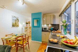 A compact kitchen with a dining area, a microwave, a sink, and a window with flowers.