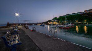 A waterfront promenade with benches, a calm harbor with boats, and a building with lights on one side. - 4 Bed in Saundersfoot (oc-pw9285) (Saundersfoot)