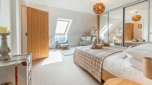 A bedroom with a large bed, a sitting area with a chair, a wardrobe, and a skylight. - 4 Bed in Saundersfoot (oc-pw9285) (Saundersfoot)