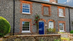 A traditional stone house with multiple windows and doors, a well-maintained garden, and a stone wall in the foreground. - 2 Bed in Weybourne (oc-2372) (Weybourne)