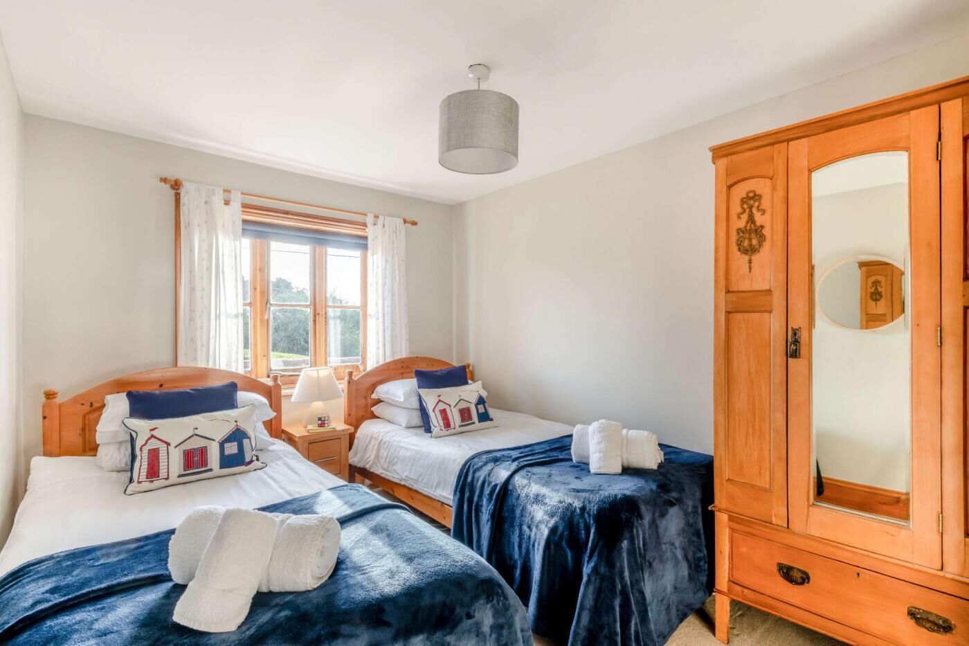 A bedroom with two beds, a wardrobe, and a window with curtains.