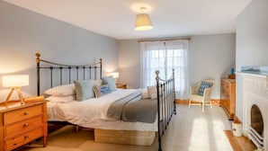A bedroom with a bed, bedside tables, a chair, a fireplace, and a window with curtains. - 2 Bed in Weybourne (oc-2372) (Weybourne)