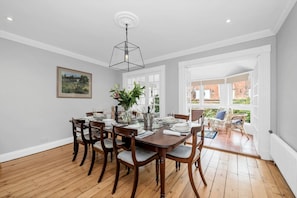 Une salle à manger avec une table en bois dressée pour six personnes, entourée de chaises, et dotée d’une grande fenêtre donnant sur l’extérieur.