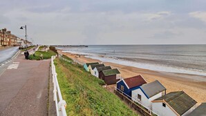 Een kustweg met een strand, een pier en kleurrijke strandhuisjes.