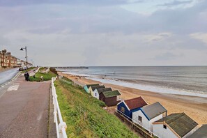 A coastal road with a beach, a pier, and colorful beach huts.