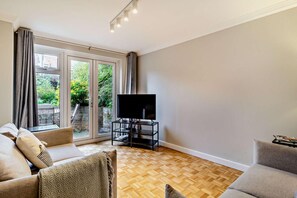 A living room with a TV on a stand, a sofa, and a large sliding glass door leading to a garden.