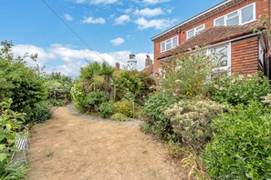 A residential garden with a pathway leading to a house with a red brick facade and a white window. - 4 Bed in Southwold (oc-stjam) (Southwold)