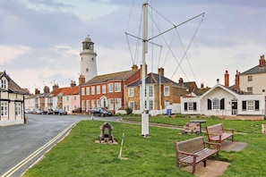 Un pueblo costero con un faro, casas tradicionales, una zona verde con bancos y una vía ferroviaria.