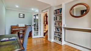 Een kamer met een piano, boekenplanken, een spiegel en een radiator.