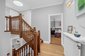 A modern interior with a wooden staircase, a white radiator, and a bedside table with a decorative bowl. - 4 Bed in Southwold (oc-stjam) (Southwold)