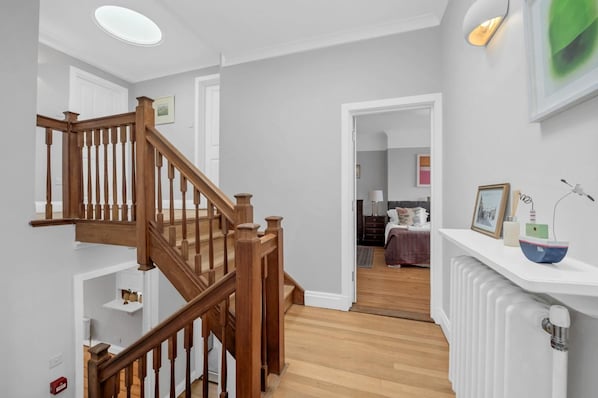 Un interior moderno con una escalera de madera, un radiador blanco y una mesita de noche con un cuenco decorativo.