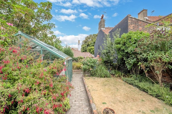 A garden with a glass greenhouse, brick walls, and a clear sky. - 4 Bed in Southwold (oc-stjam) (Southwold)