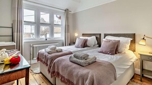 Een slaapkamer met twee bedden, een raam, een radiator, een nachtkastje en een lamp.
