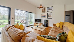A modern living room with a large sofa, a coffee table, and a TV. There are large windows and a door leading to a patio. - 2 Bed in Beckley (oc-rh1176) (Beckley)