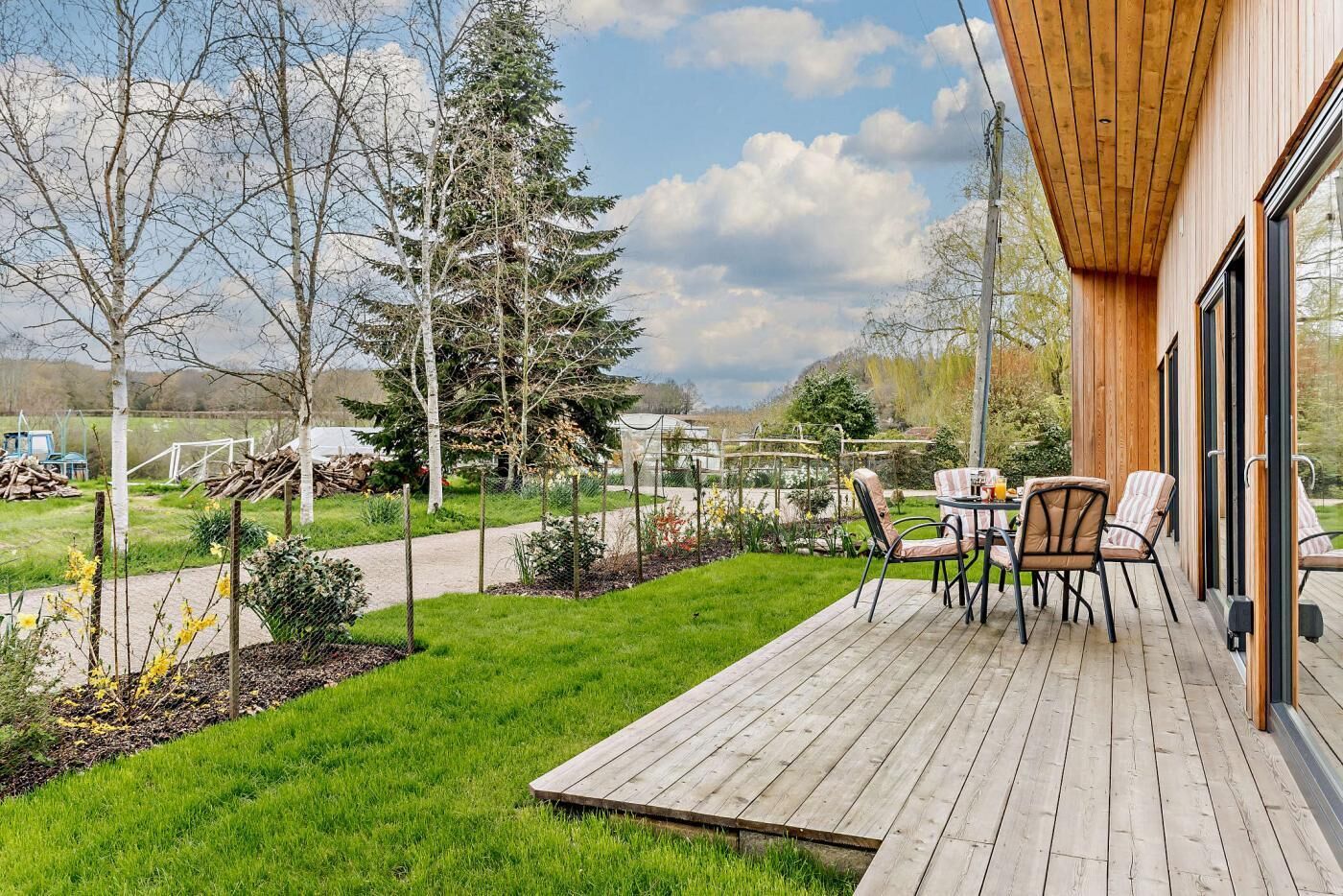 A wooden deck with outdoor seating, a view of a garden, and a building with large windows.