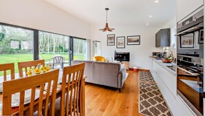 A modern kitchen with a dining area, large windows, and a view of the outdoors.