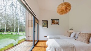A bedroom with two beds, a large window, and a view of trees and grass.