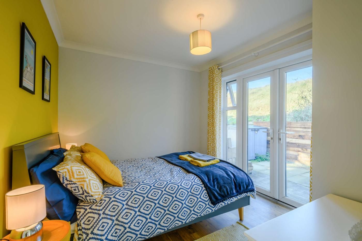 A bedroom with a bed, a bedside lamp, a window with a view, and a door leading to an outdoor area.