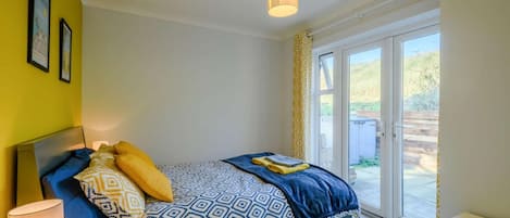 A bedroom with a bed, a bedside lamp, a window with a view, and a door leading to an outdoor area.