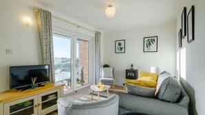 A living room with a television, sofa, armchair, and a small table with a lamp. - 2 Bed in Eccles-on-Sea (oc-a27194) (Eccles-on-Sea)
