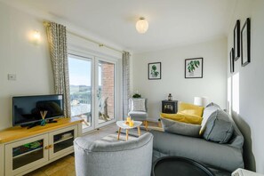 Ein Wohnzimmer mit Fernseher, Sofa, Sessel und einem kleinen Tisch mit Lampe.