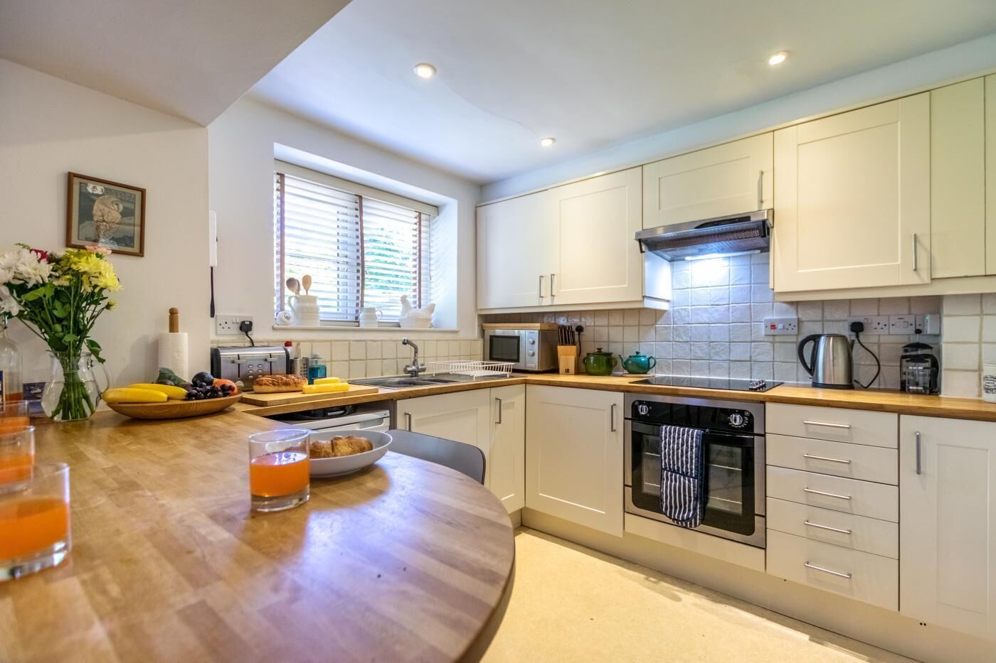 A modern kitchen with white cabinets, a wooden countertop, a built-in oven, and a window with blinds.