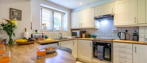 A modern kitchen with white cabinets, a wooden countertop, a built-in oven, and a window with blinds.