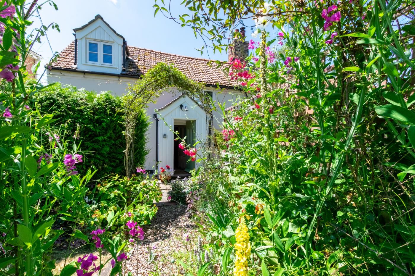 A garden with a white building, a pathway, and various plants and flowers.