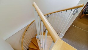 Un escalier en colimaçon en bois, avec des balustrades blanches et une main courante en bois.