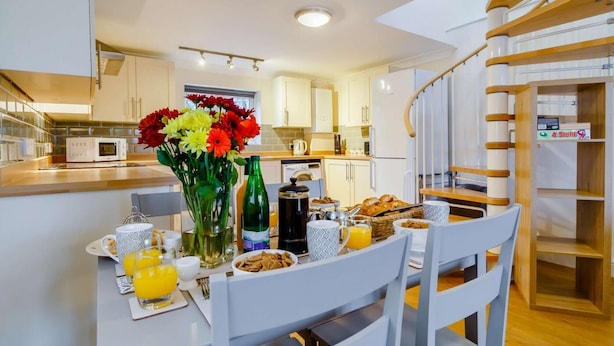 Une cuisine moderne avec des meubles blancs, une table à manger dressée pour le petit-déjeuner et un escalier avec des rampes en bois.