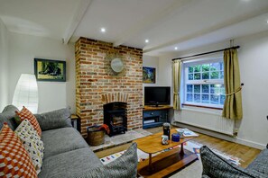 Una sala de estar con chimenea de ladrillo, televisión, sofá y ventana con cortinas.