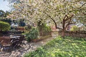 Eine Terrasse mit einem runden Tisch und Stühlen, umgeben von üppiger Vegetation und blühenden Bäumen.