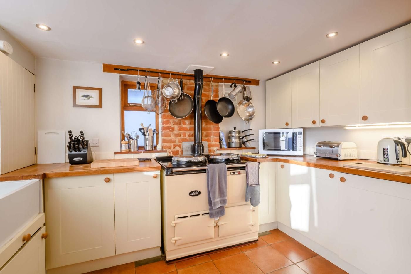 A kitchen with white cabinets, a stove, a microwave, and hanging pots.