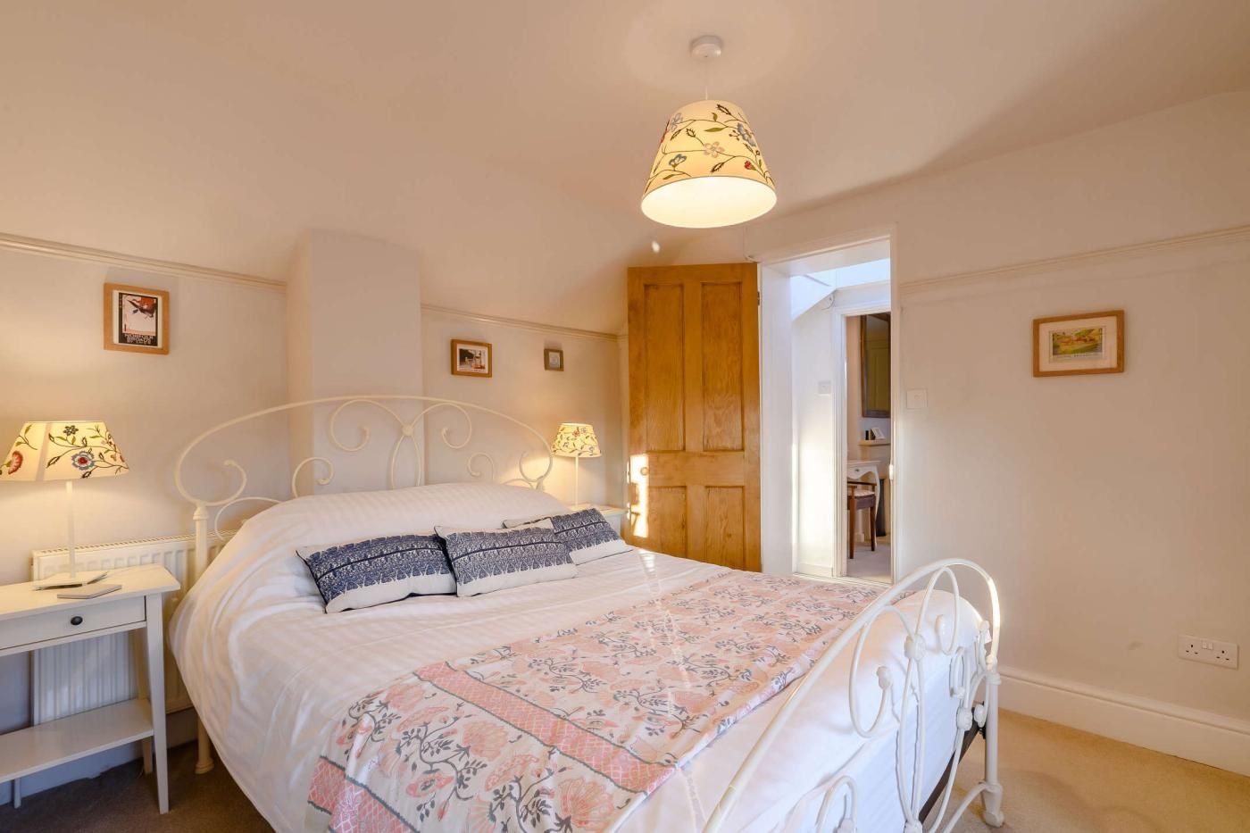 A neatly arranged bedroom with a bed, bedside lamps, a nightstand, and a door leading to another room.