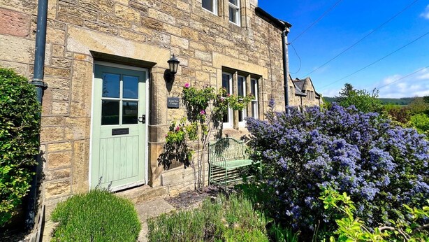 A stone building with a green door, a bench, and a sign that reads "Lime Tree Cottage." - 2 Bed in Chatton (oc-r27205) (Chatton)