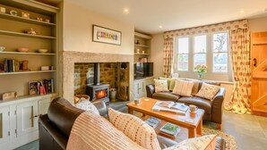 A cozy living room with a fireplace, leather sofa, wooden shelves, and a television. - 2 Bed in Chatton (oc-r27205) (Chatton)