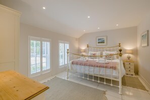 Une chambre à coucher avec un lit à baldaquin blanc, deux tables de chevet, un banc en bois et une fenêtre avec des stores.