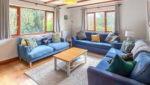 A cozy living room with two sofas, a coffee table, and large windows with curtains. - 4 Bed in Tenby (oc-vv27177) (Manorbier)