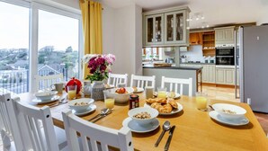 A dining area with a table set for breakfast, a view of the kitchen, and a balcony with a view of the neighborhood. - 4 Bed in Tenby (oc-vv27177) (Manorbier)