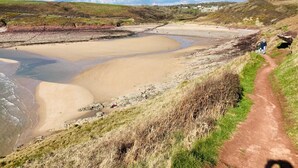 A coastal landscape with a sandy beach, a dirt path, and a person walking. - 4 Bed in Tenby (oc-vv27177) (Manorbier)